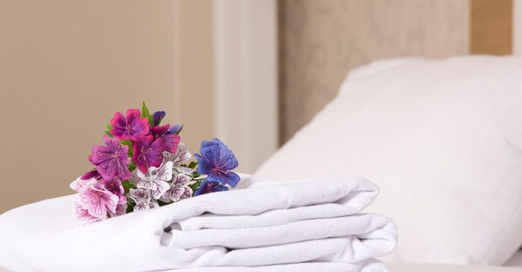 Cozy hotel room featuring stacked white towels and vibrant flowers for a welcoming touch.