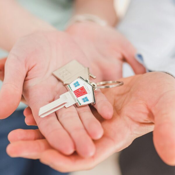 Close-up of hands holding a key with a house-shaped keychain, symbolizing new beginnings.