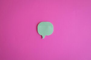 A simple green speech bubble cutout on a vibrant pink background, perfect for creative designs.